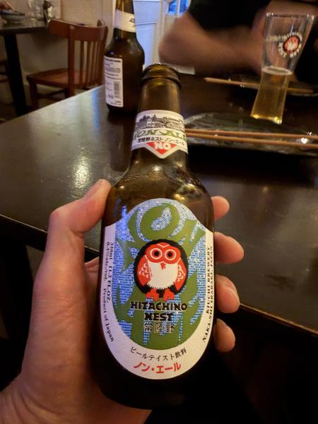 This photo captures a hand holding a bottle of Hitachino Nest beer at a dimly lit restaurant in Koningsstraat, Nieuwmarktbuurt, Amsterdam